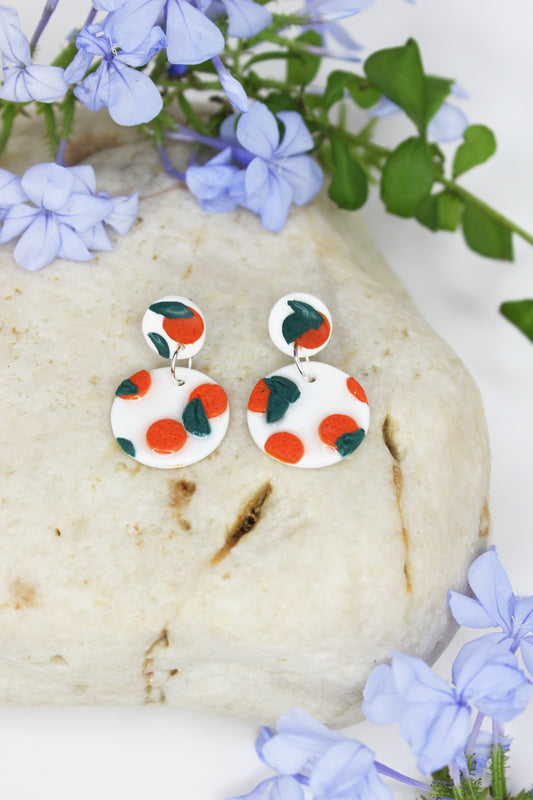 Boucles d'oreilles blanches vernies avec oranges sculptées, inspirées des agrumes de la Méditerranée. Entièrement fabriquées à la main sur la Côte d'Azur, en argile polymère, résine et argent plaqué.