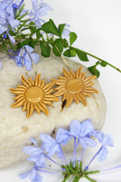 Boucles d'oreilles créoles avec pendentif  en forme de soleil, de couleur dorée, en argile polymère et acier inoxydable doré. Fabriquées à la main sur la Côte d&#39;Azur